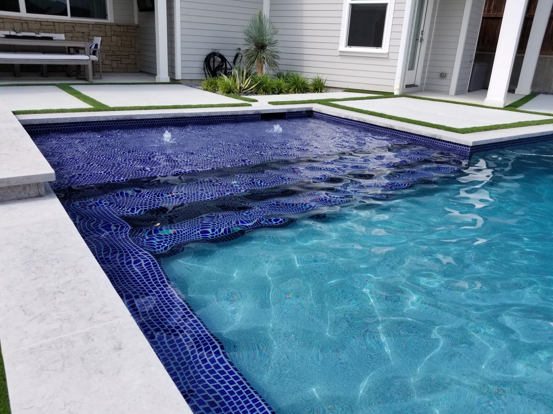 New glass tile steps and fountains in a remodeled backyard pool